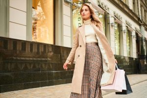 Imagem Mulher loira estilosa de casaco bege com sacolas de compras andando na rua da cidade