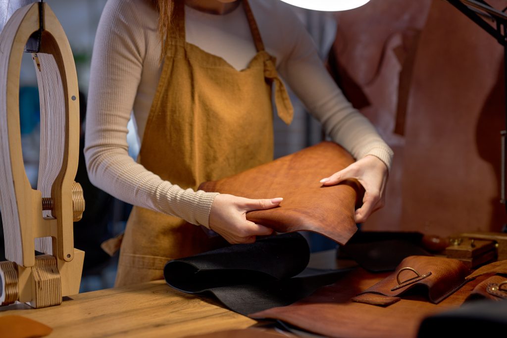  Jovem artesã segurando couro, preparando-se para costurar uma bolsa com ele. 